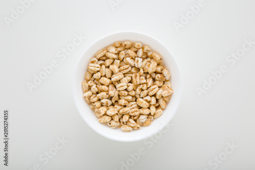 Obraz na plátně Full white bowl of yellow dry puffed wheat flakes on light gray table background
