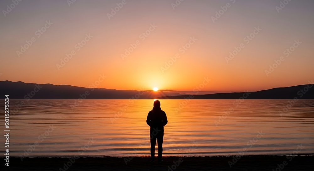 Obraz premium Man watching serene sunset over water.