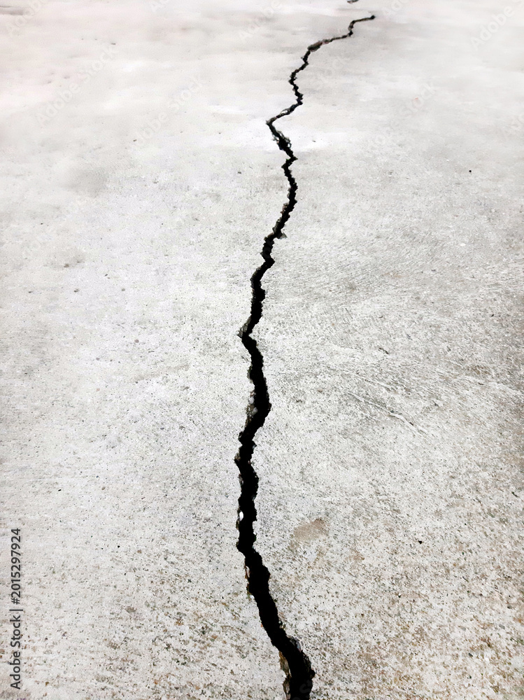 Fototapeta premium Gray cement floor texture with a vertical crack in perspective in the middle, vertical photo.