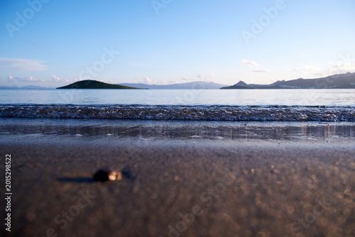 Coastal landscape featuring gentle waves and an island under a clear sky