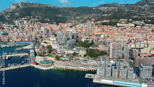 4K aerial view of Monte-Carlo Casino with green domes, Port Hercule superyacht marina, dense residential towers and Tête de Chien rocky cliff above the principality of Monaco.
