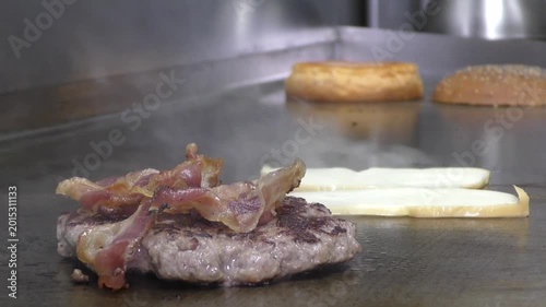 Preparazione di un panino hamburger su piastra. Panino hamburger grigliato con pancetta, cipolla glassata, formaggio e uova