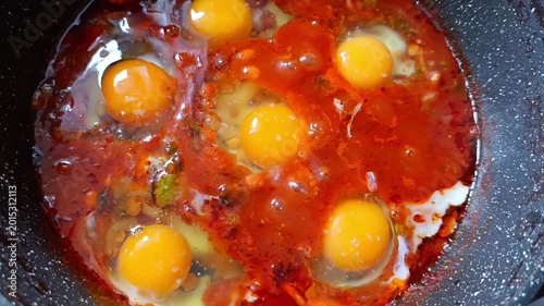 Cooking shakshuka with chicken eggs, chickpeas and tomato sauce in a frying pan. Middle Eastern and African meal