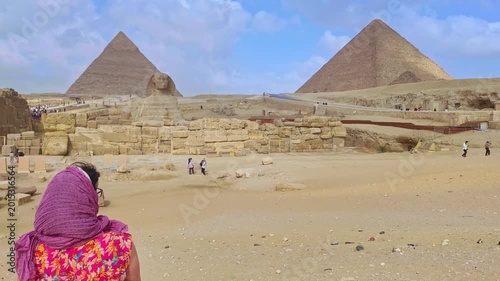 Slow motion view of a woman with a headscarf looking at the great sphinx and the pyramids of giza. Famous historical landmark in the desert