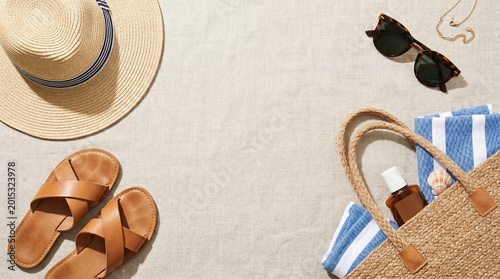 Beach essentials arranged for a relaxing summer vacation, capturing the essence of a serene getaway. The scene features a hat, sunglasses, sandals, bag, and other accessories. 