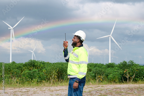 Technician communicating via a walkie talkie, overseeing wind turbines and a rainbow. A symbol of sustainable energy