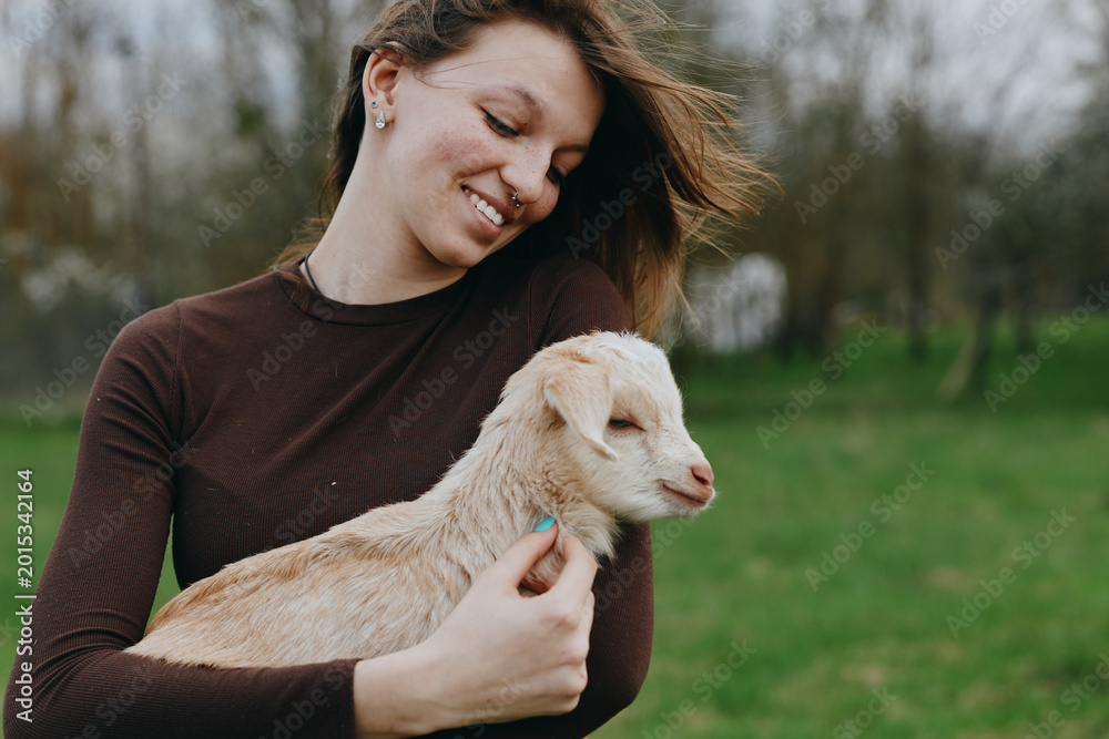 Fototapeta premium Goat, kid, woman, outdoor, lifestyle, nature, countryside, portrait, smiling, affection in a sunlit moment as a gentle breeze moves through greenery and calm happiness in a pastoral setting