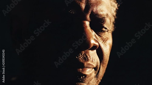 Close up extreme portrait of an elderly Black man, face illuminated by harsh side light, deep shadows, showing weathered skin texture and thoughtful expression