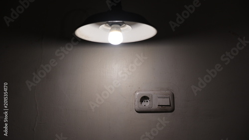Photos A glowing lamp lights a wall outlet and switch, creating soft shadows in a minimalist interior setting