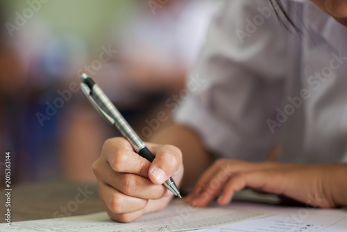 Close up hand of students reading and taking exam sheets exercises answer with stress in classroom