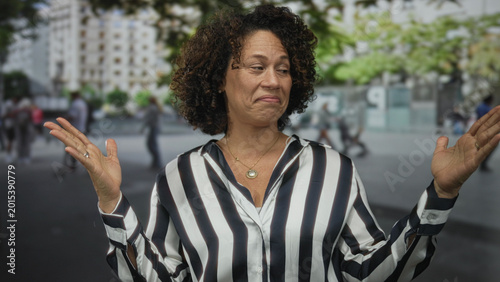 Bild auf Leinwand Woman holds hands up on street wearing black and white striped shirt under city plaza buildings; uncertainty doubt hesitation perplexity