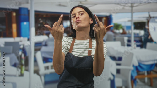 Canvas Print Woman in apron flips middle finger inside building dining area, hands raised with stern face and visible forearms; defiance rebellion