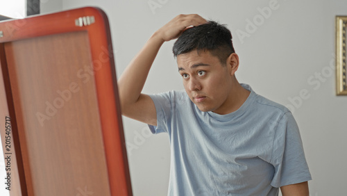 Photos Man in t shirt pulls at collar and fixes hair while facing a wooden mirror and framed art in studio; grooming calm