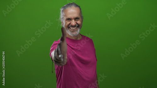 Schilderij op canvas Man with long hoary hair offering right hand for handshake in green studio wearing magenta tshirt and bracelets; welcoming greeting