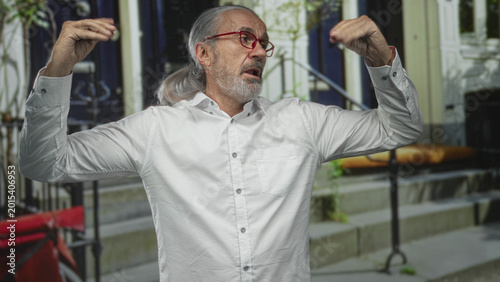Canvastavla Man raising both hands in a measured gesture on a building stoop wearing red glasses and a white shirt; quiet contemplation