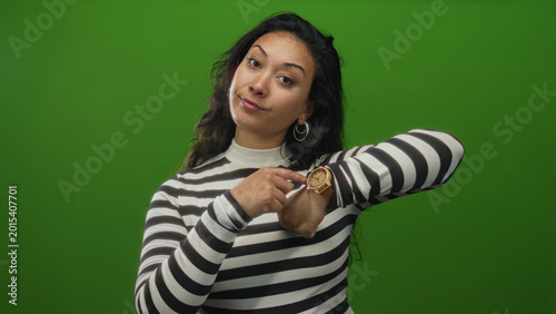 Photos Woman points finger to wristwatch in studio with green backdrop; impatience time punctuality reminder
