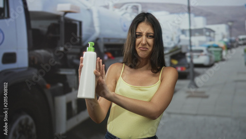 Schilderij op canvas Woman holds white pump bottle at arm's length and pushes it away on street near parked trucks; disgust caution