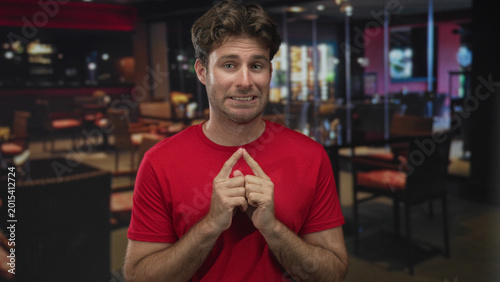 Photos Man with fingertips touching and awkward smile in building restaurant interior; nervousness hesitation uncertainty