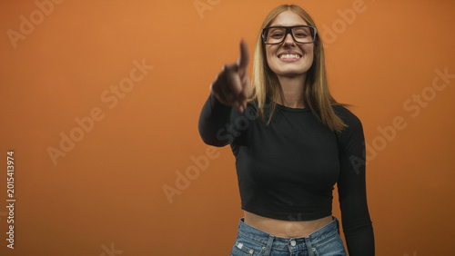 Foto Woman points finger to camera showing smiling face and exposed midriff while wearing glasses and jeans in studio; playful confidence