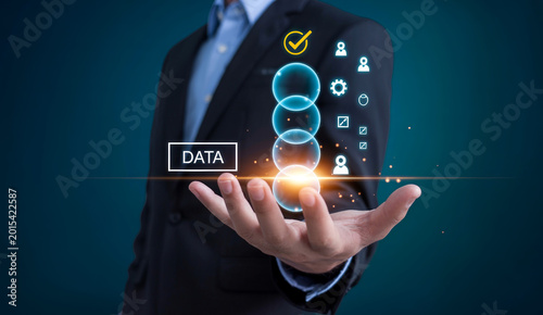 Businessman holding glowing data bubbles with check mark and analytic icons over dark blue background.