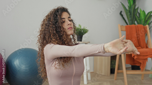 Fotografía Woman stretches hands forward and grasps wrist in a yoga studio with exercise ball, chair and houseplant visible; serenity mindfulness