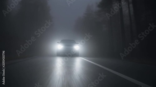 A car's bright headlights illuminate a dense, mysterious fog on a dark, empty road, creating a challenging and low-visibility driving experience through an atmospheric natural phenomenon
