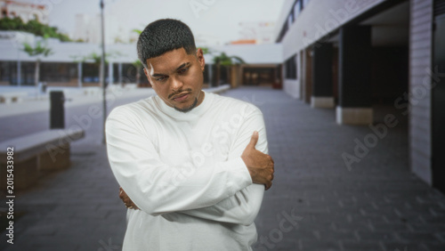 Cuadro en lienzo Hispanic man in white long sleeve shirt grips his arm, grimacing and holding elbow near concrete benches outside a commercial building plaza; discomfort