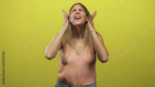 Bild auf Leinwand Woman pressing temples with both hands and grimacing, eyes closed in studio with yellow backdrop; headache frustration
