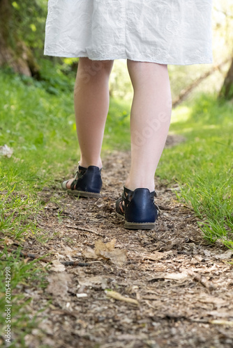 Back view of young girl walking along narrow forest trail in soft sunlight. Legs
