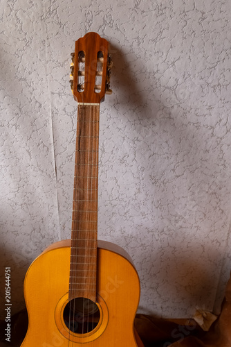 Quadro em tela Beautiful wooden guitar resting against a textured wall, waiting for the strum o