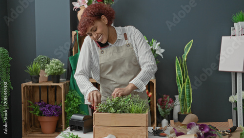 Quadro su tela Woman florist arranging potted plants with hands and phone to cheek in building; careful multitasking calm
