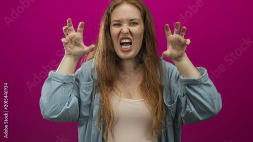 Fotografía Woman with bared teeth snarling with raised hands in pink studio; anger defiance intensity ferocity