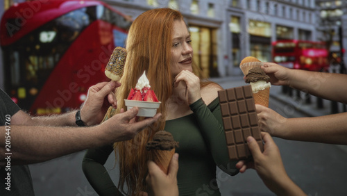 Fotografie Woman touching chin hesitates as multiple hands offer ice cream cones and a chocolate bar on a busy street; indecision temptation