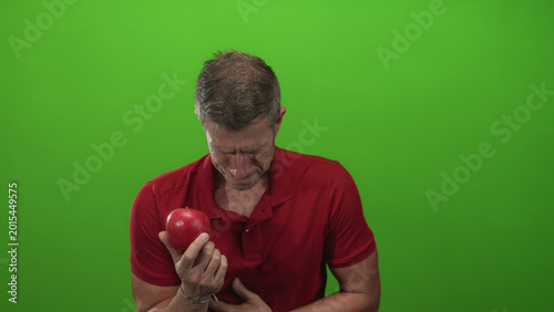 Foto Man holding red apple clutching chest for heartattack in studio with green background; concern health