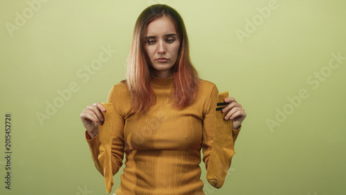 Fotografie Young redhead woman holding two yellow socks by the cuffs with arms extended, wearing mustard sweater, studio; melancholy resignation