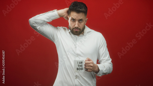 Foto Man with beard holds 'i am the boss' mug and shrugs left hand in studio red backdrop, wearing white shirt and gripping the cup; wry resignation