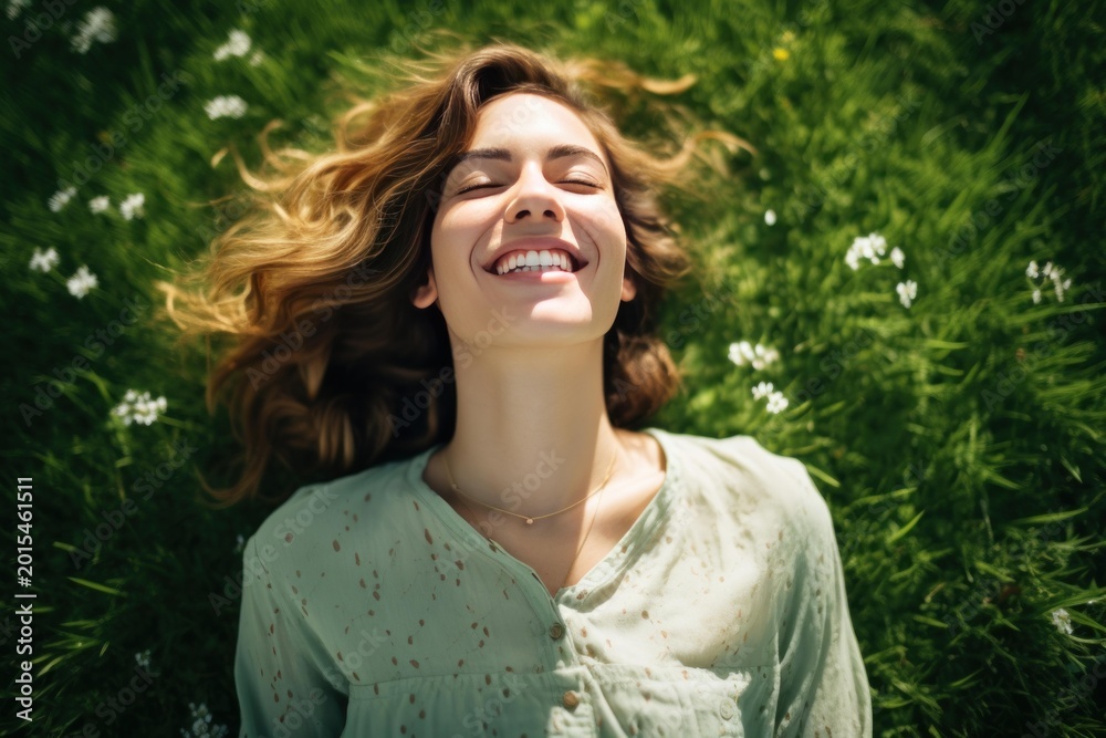 Fototapeta premium Young woman lying on green grass smiling with closed eyes, enjoying nature and sunlight