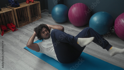 Foto Man on blue mat doing bicycle crunches with hands behind head and knees raised, socks on, exercise balls nearby in studio; fitness focus wellness