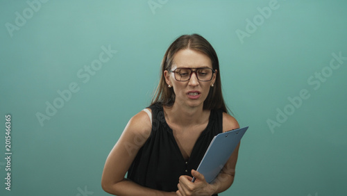 Fotografia Woman wearing glasses holding a blue clipboard and grimacing while clutching it to her chest in teal studio; disgust