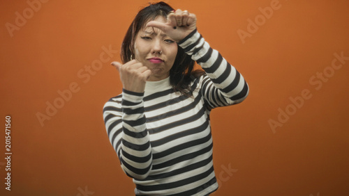 Cuadro en lienzo Woman points thumb to self while singing with open mouth and striped sweater in studio; playful confidence
