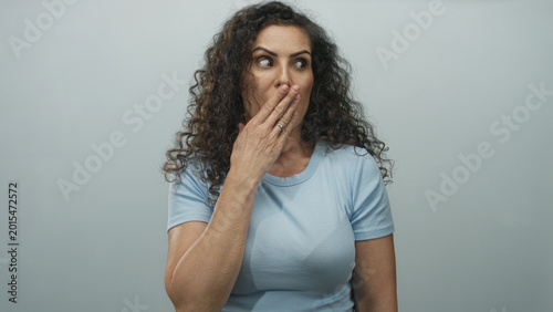 Obraz na płótnie Woman covers her mouth with hand against gray wall in studio in light blue shirt in silence gesture; shock
