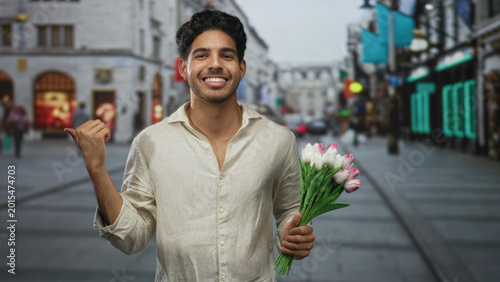 Photos Man holding a bouquet of tulips on a pedestrian shopping street, smiling with eyes closed and wearing a beige linen shirt while gently gripping stems; romance joy