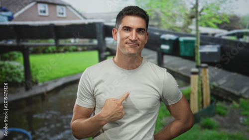 Tableau sur toile Man points finger to chest on street in amsterdam wearing short sleeve t shirt in outdoor canal setting; pride