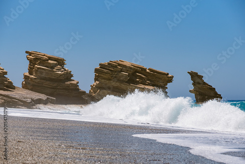 Fotografi Landscape with waves crashing against characteristic rocks on Triopetra Beach on