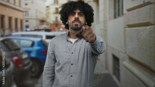 Fotografía Man points finger at camera on street, curly hair and beard visible; confrontation anger accusation