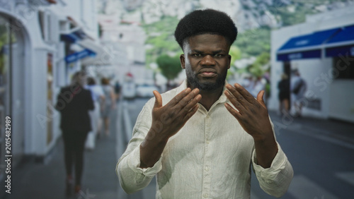 Foto Man buttoning pale linen shirt with hands and clenched jaw while tightening collar on busy pedestrian street with blurred crowd; frustration preparation