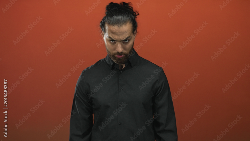 Fototapeta premium Man with beard wearing a black shirt and closed eyes looking down in an orange studio midshot; introspective calm.