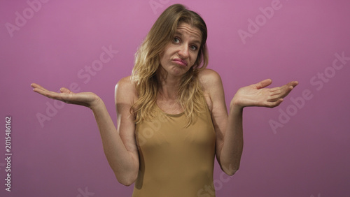 Photos Woman shrugging with palms up and raised shoulders in studio against pink backdrop in a tan sleeveless top; uncertainty