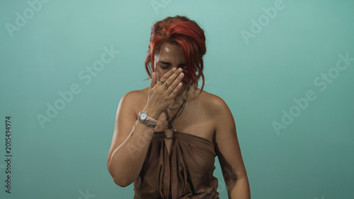 Fotografie Woman covering face with hands in studio teal backdrop showing bare shoulders and red hair visible; vulnerability sadness
