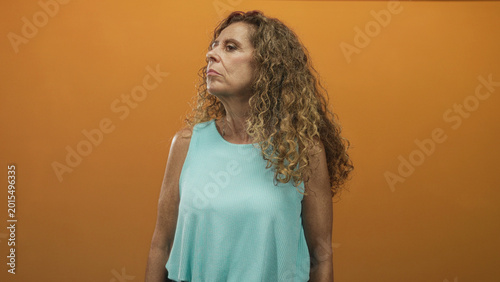 Photography Woman profile with head turned left, bare shoulder visible and curly hair, standing in studio orange backdrop; contemplative reflection solitude